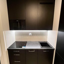 Frans meble - Nowoczesna, kompaktowa kuchnia w czerni z białym marmurowym backsplash, wbudowaną kuchenką elektryczną, mikrofalówką Amica i czarnym zlewem.