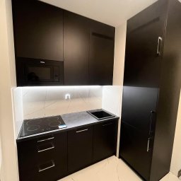 Frans meble - Czarna, matowa kuchnia na wymiar z piekarnikiem Amica, płytą indukcyjną i białym blatem z marmurowym wzorem, oświetlona ledowym światłem.