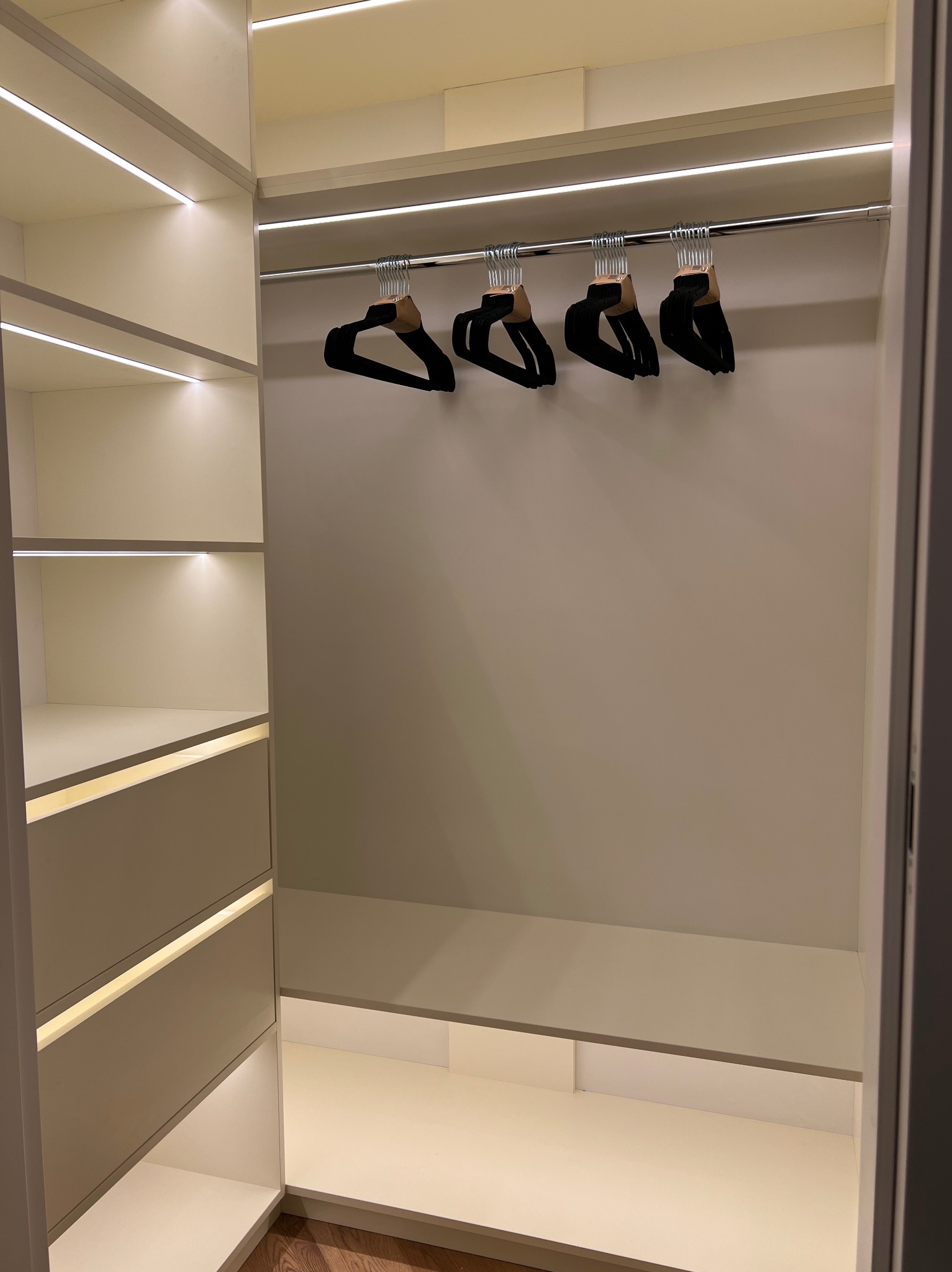 Wnętrze jasnej garderoby z oświetleniem LED, puste półki i wieszaki na ubrania