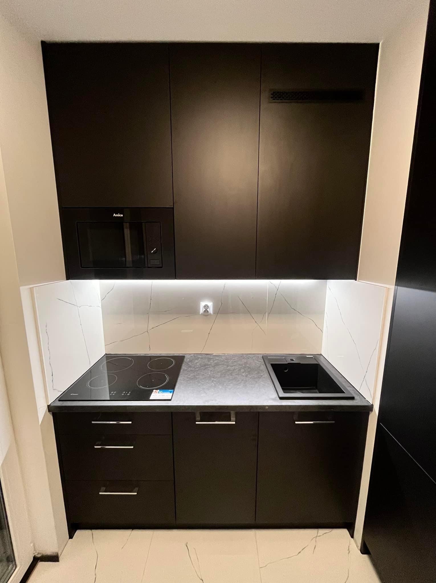 Nowoczesna, kompaktowa kuchnia w czerni z białym marmurowym backsplash, wbudowaną kuchenką elektryczną, mikrofalówką Amica i czarnym zlewem.