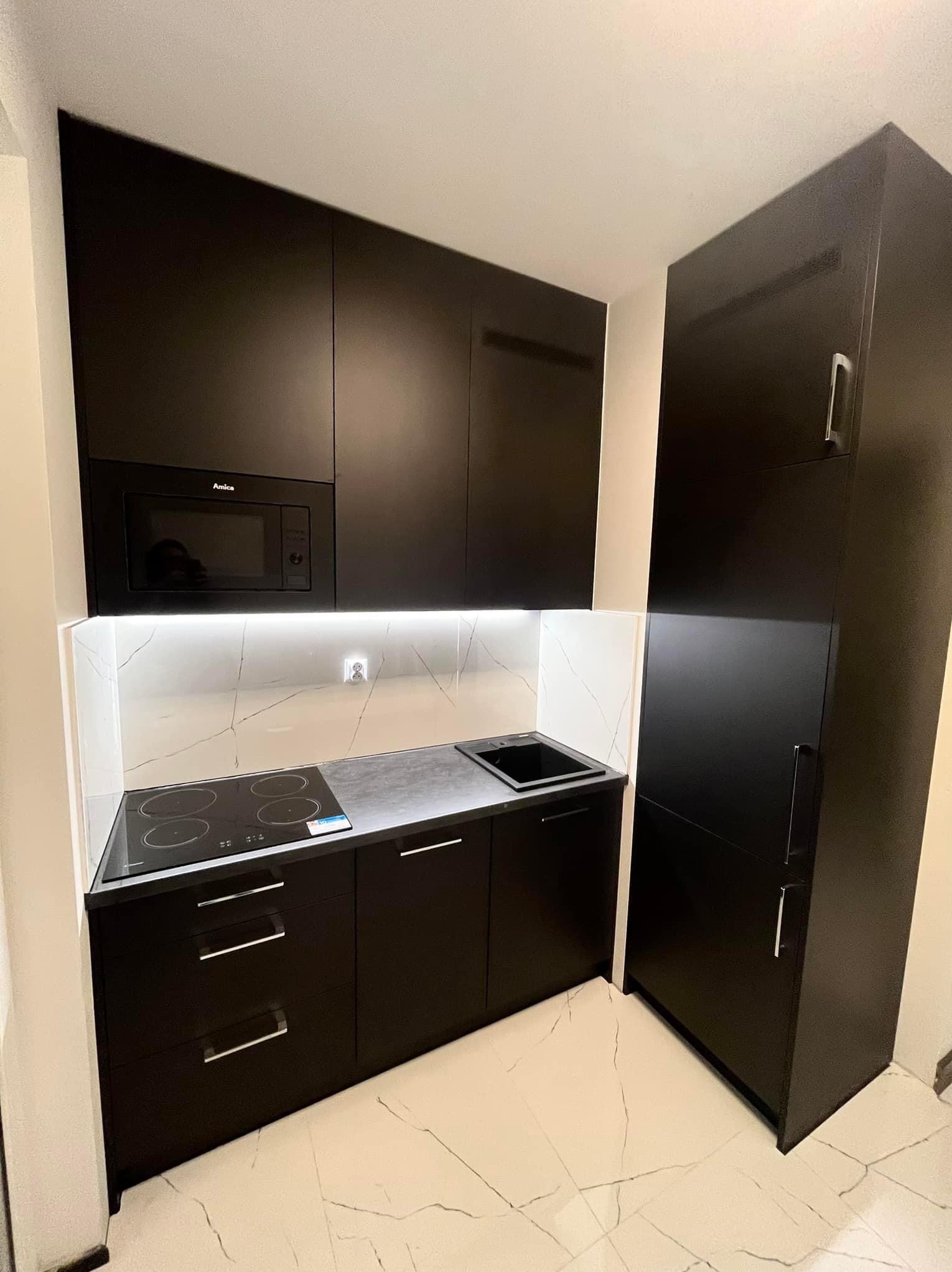 Czarna, matowa kuchnia na wymiar z piekarnikiem Amica, płytą indukcyjną i białym blatem z marmurowym wzorem, oświetlona ledowym światłem.