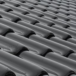 Marcin Dom - Błyszczące, czarne dachówki ceramiczne ułożone rzędami na dachu, widoczne krople deszczu.