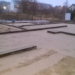 Marcin Dom - Przygotowanie gruntu pod fundamenty domu: ubijanie piasku zagęszczarką w szalunkach, w tle zabudowa jednorodzinna.