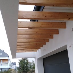 Marcin Dom - Drewniana pergola nad wjazdem do garażu w nowoczesnym domu jednorodzinnym, widok od dołu, w tle zabudowa osiedlowa i zieleń.