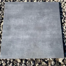 Pojedyncza, kwadratowa płyta podłogowa w odcieniach szarości z delikatną teksturą, ułożona na podłożu z drobnych kamieni.