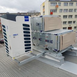 Marek Felskowski Coldest Group - System klimatyzacji MRV5 Haier zainstalowany na dachu budynku wielorodzinnego, widoczne jednostki zewnętrzne i moduły wentylacyjne z zabezpieczeniami kartonowymi, pochmurne niebo w tle.