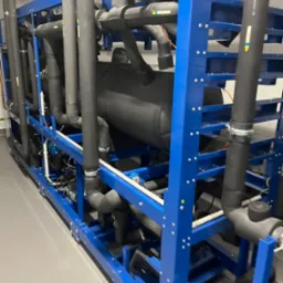 Kompleksowa instalacja chłodnicza z rurami w izolacji, zamontowana na niebieskiej ramie, widok z boku.