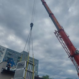 Marek Felskowski Coldest Group - Montaż centrali wentylacyjnej na dachu budynku za pomocą dźwigu KROPF-BA, pracownik nadzoruje proces, widoczna klimatyzacja zewnętrzna LG na ścianie budynku.