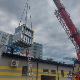 Marek Felskowski Coldest Group - Montaż centrali wentylacyjnej na dachu budynku przy użyciu dźwigu Kropf-BA, widoczni dwaj pracownicy na dachu i drabina oparta o budynek.