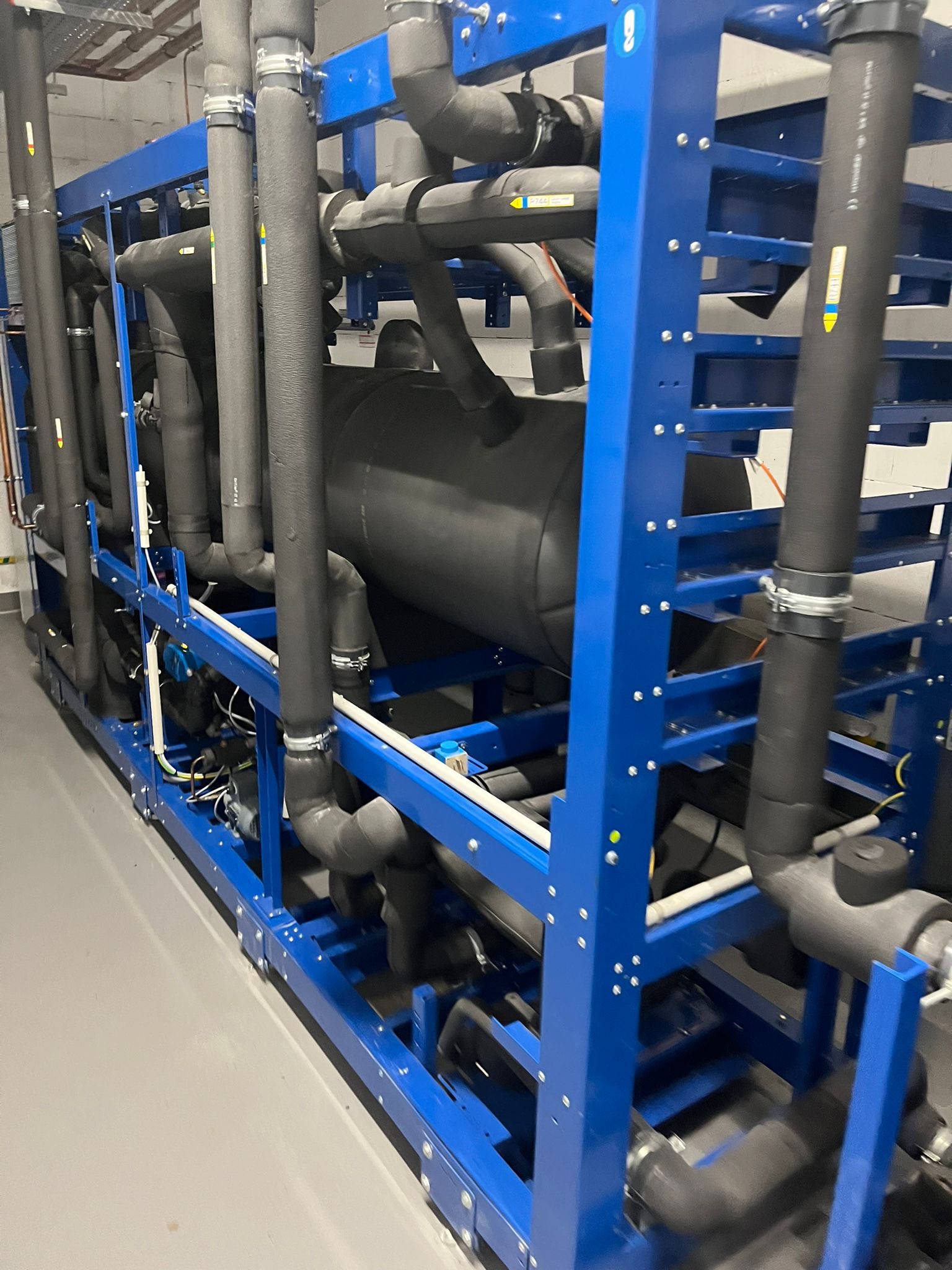 Kompleksowa instalacja chłodnicza z rurami w izolacji, zamontowana na niebieskiej ramie, widok z boku.