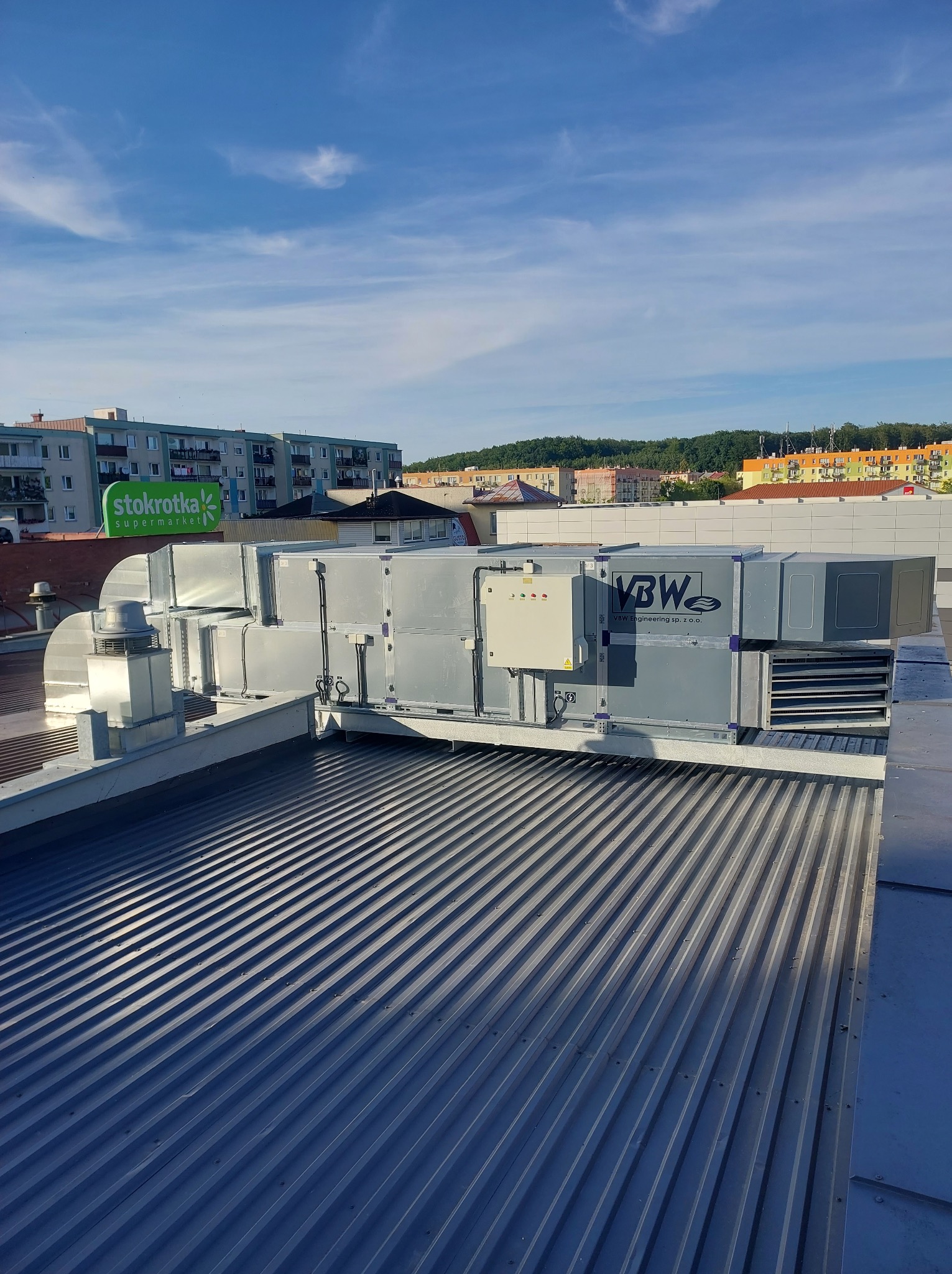 Instalacja wentylacyjna na dachu budynku z widocznym logo firmy VBW Engineering sp. z o.o., na tle zabudowań miejskich i błękitnego nieba.