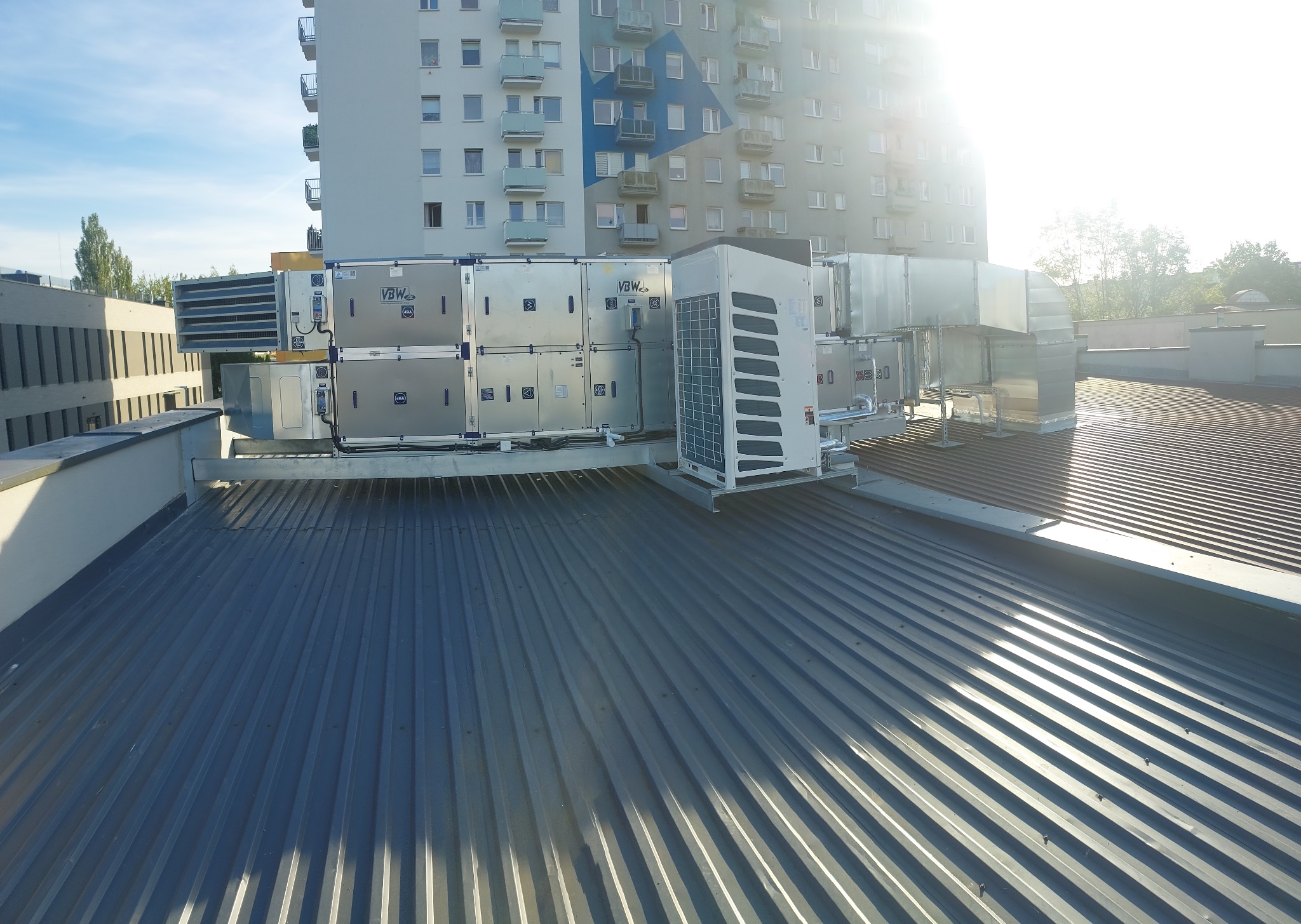 Instalacja wentylacyjna i klimatyzacyjna na dachu budynku wielorodzinnego, widoczne kanały wentylacyjne, jednostki zewnętrzne klimatyzacji i centrala wentylacyjna VBW, oświetlone silnym światłem...