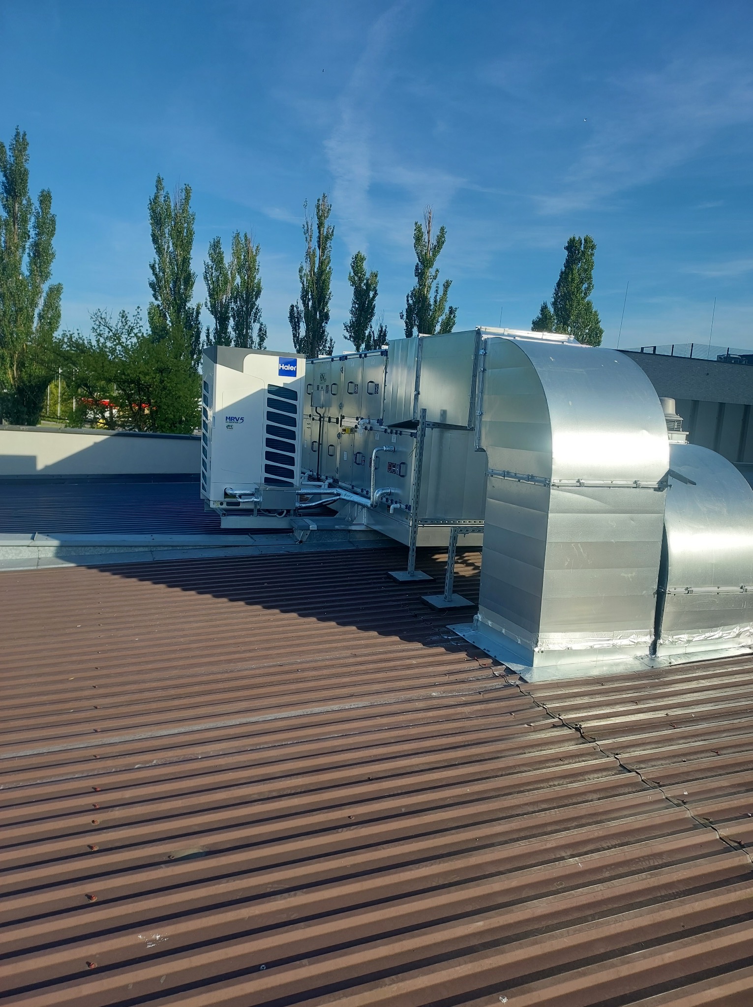 System klimatyzacji Haier MRV5 z kanałami wentylacyjnymi na dachu budynku w słoneczny dzień.