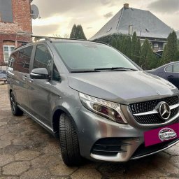 Detailing Olivier Marciniak - Szary Mercedes-Benz V-klasa zaparkowany na brukowanej nawierzchni przed budynkiem z cegły w pochmurny dzień.
