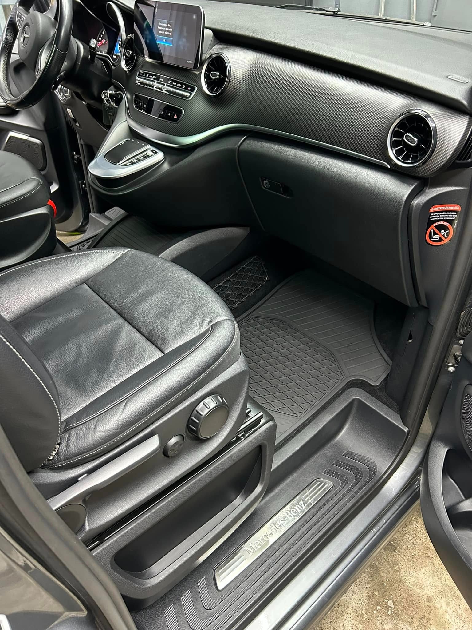 Wnętrze samochodu Mercedes-Benz z czarną skórzaną tapicerką fotela kierowcy, teksturowaną deską rozdzielczą i gumowymi dywanikami podłogowymi.