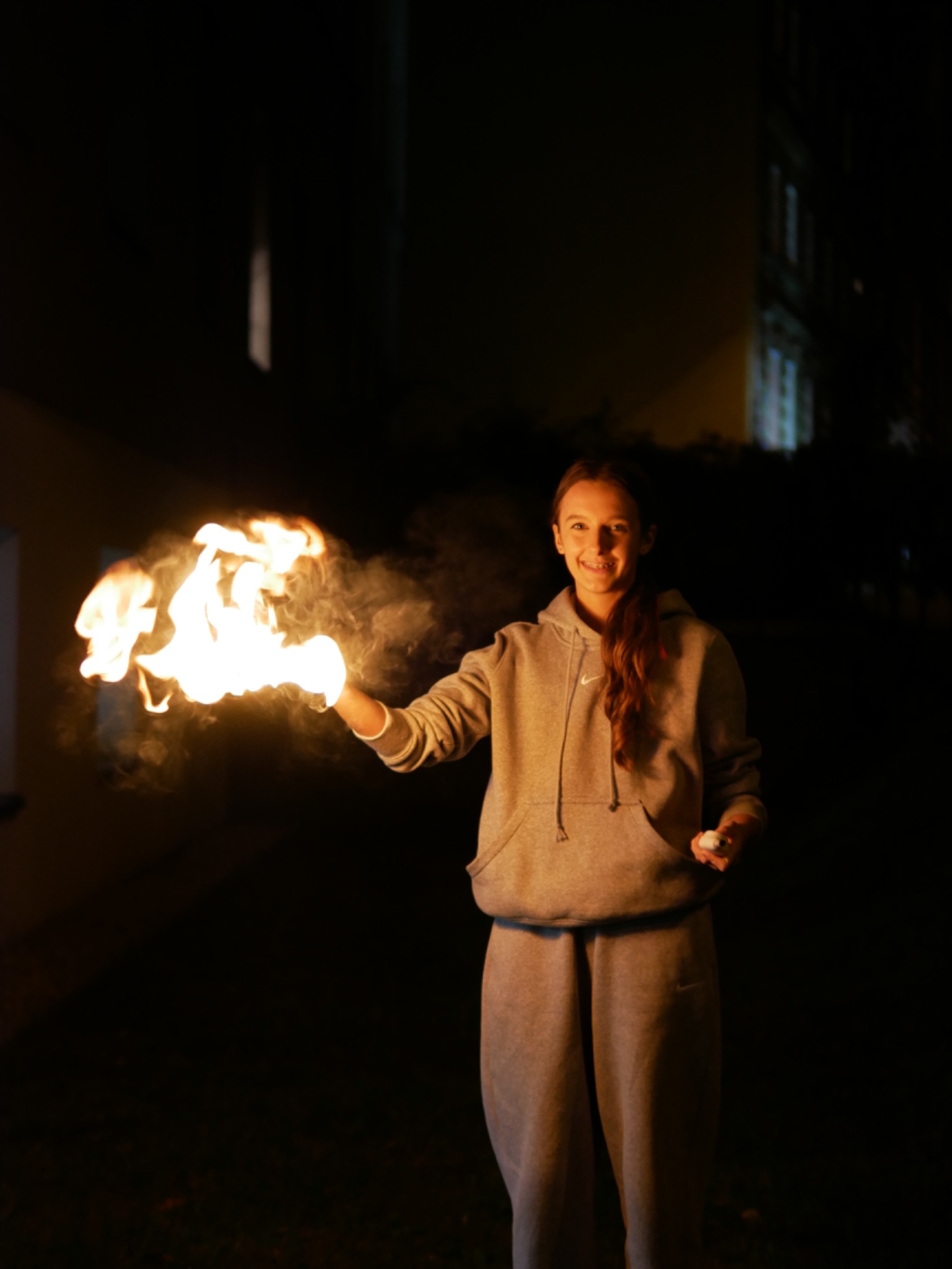 Młoda kobieta w dresie trzymająca w dłoni płonący ogień na tle nocnego nieba i budynku.