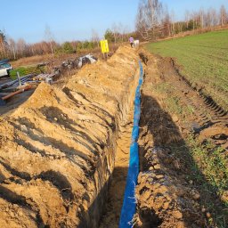 Nowoczesne technologie oze - Wykop pod instalację w Lublinie z niebieską rurą, widok z góry na wykopaną ziemię i częściowo zielone pole w tle.