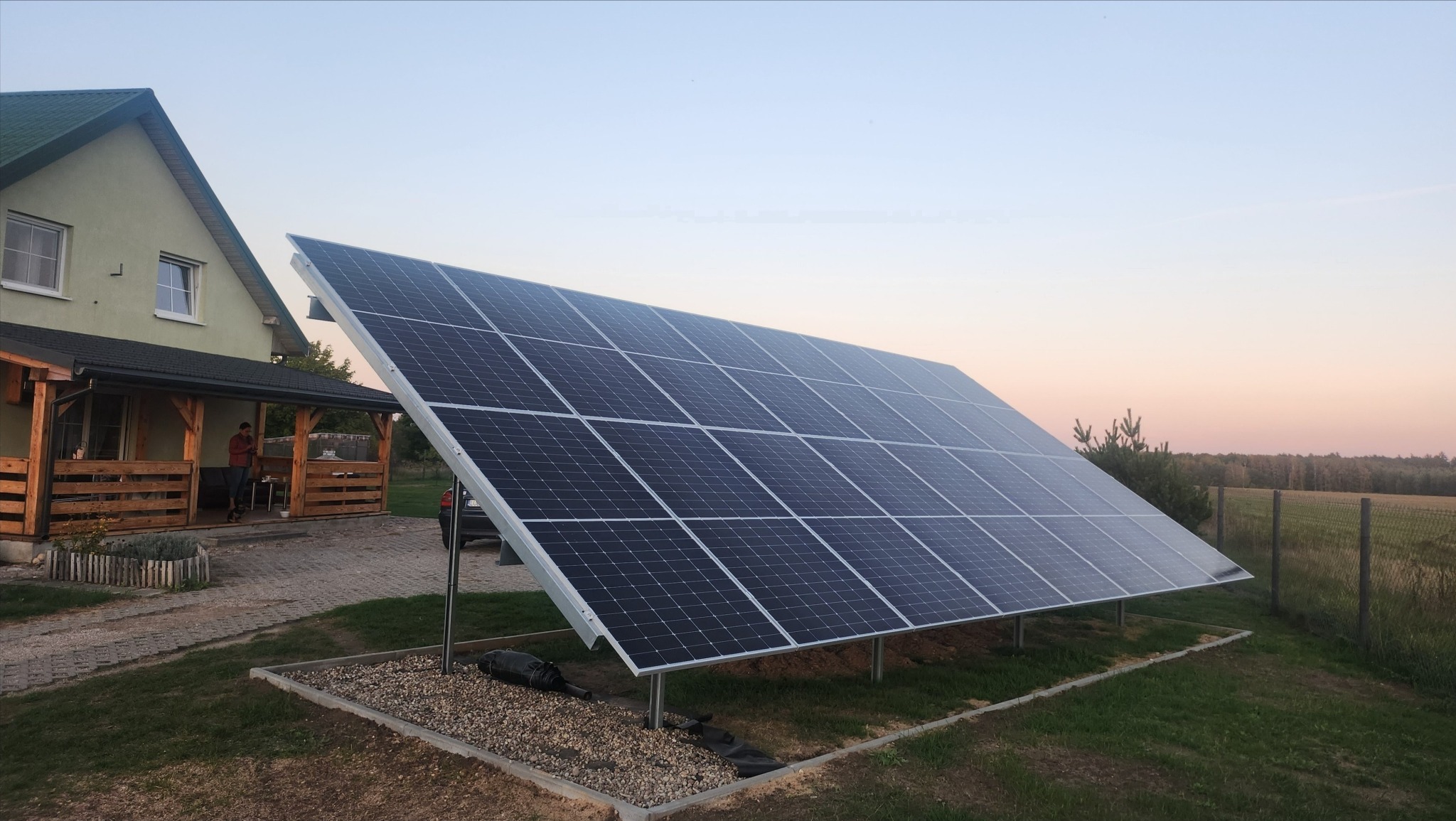Instalacja paneli słonecznych w Lublinie, widok na dom z werandą w tle, wieczorny krajobraz.