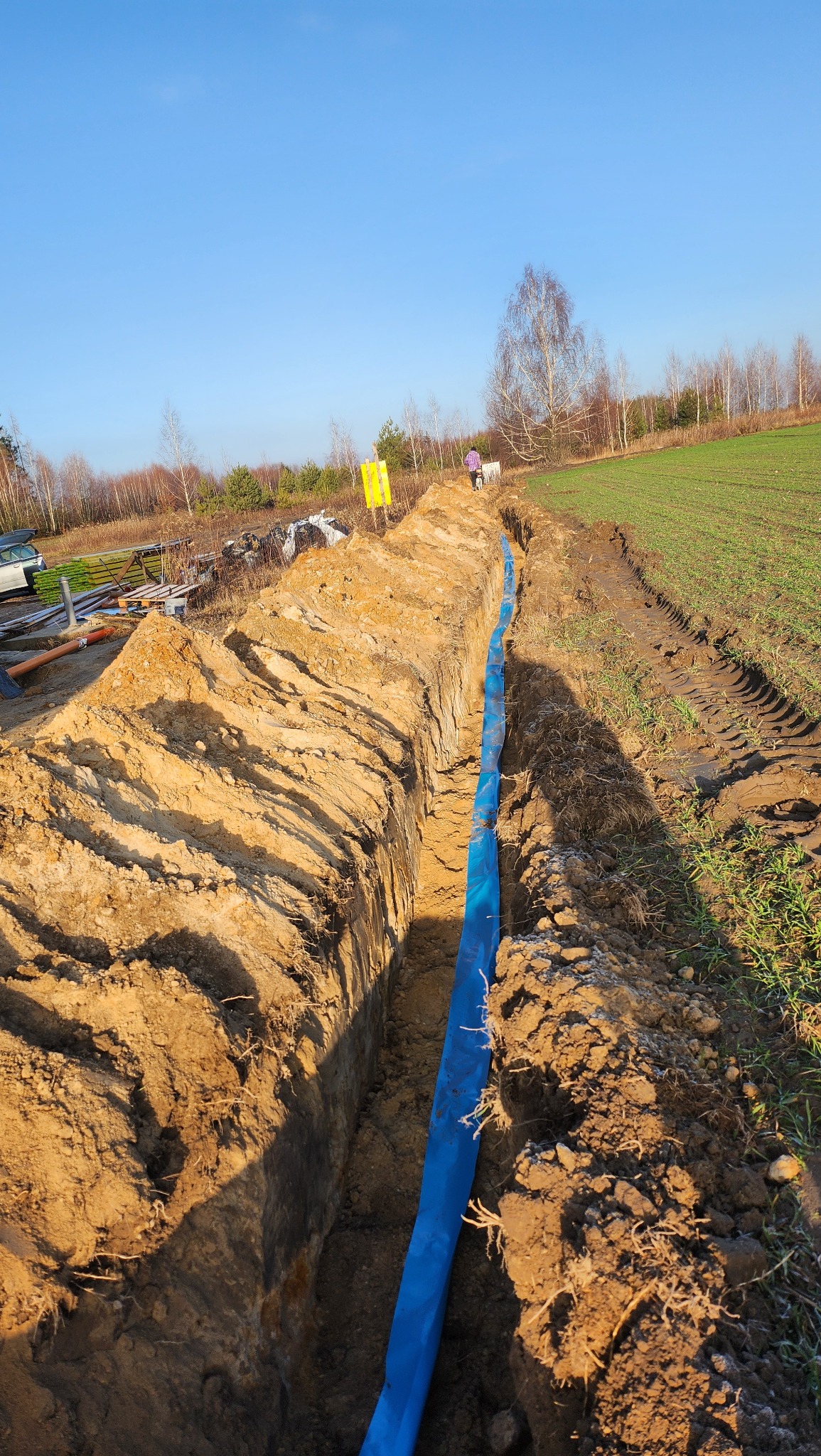 Wykop pod instalację w Lublinie z niebieską rurą, widok z góry na wykopaną ziemię i częściowo zielone pole w tle.