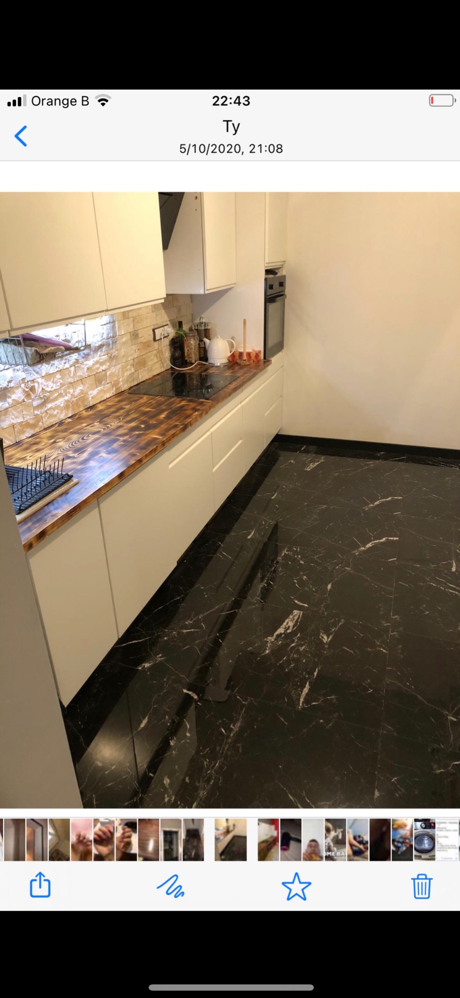 Kuchnia z białymi szafkami, blatem z ciemnego drewna i czarną marmurową podłogą, widok z perspektywy