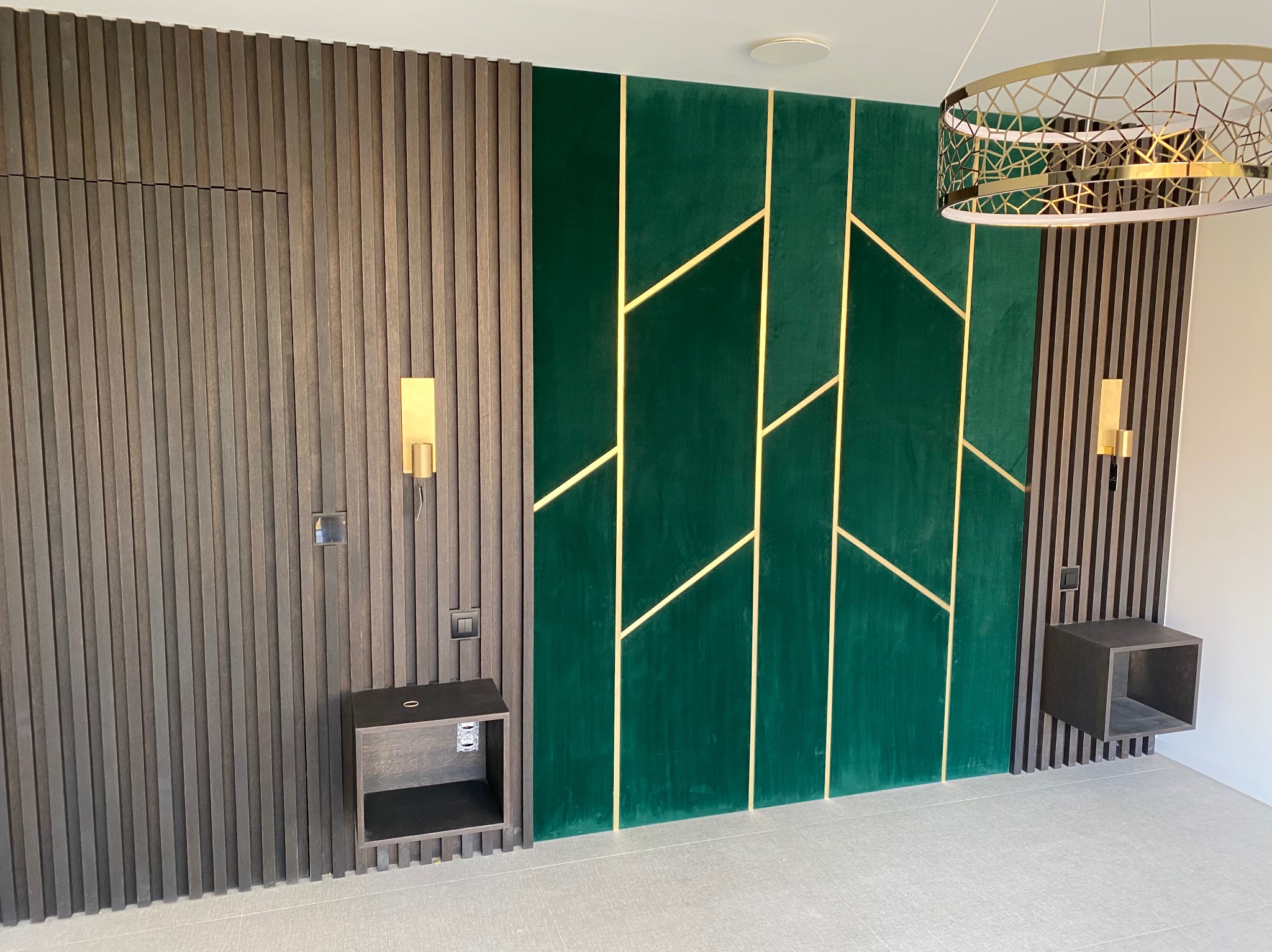 Nowoczesna aranżacja ściany z drewnianych paneli, zielonego weluru z złotymi wstawkami i wiszącej szafki nocnej, oświetlona designerską lampą.