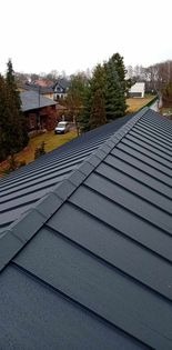 Szary dach z blachy na tle zabudowy jednorodzinnej w pochmurny dzień.