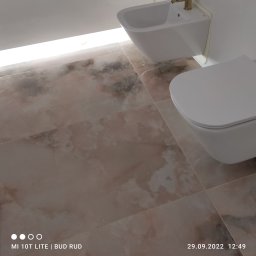 Bud Rud - Beżowe płytki podłogowe imitujące marmur w łazience, z widocznym białym bidetem i toaletą podwieszaną, oświetlenie LED pod sufitem.