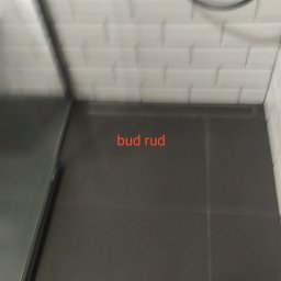 Bud Rud - Ciemnoszare płytki podłogowe w łazience z białymi, wypukłymi płytkami na ścianie i widocznym odpływem liniowym.