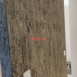 Bud Rud - Ściana z dekoracyjną fakturą w odcieniach brązu i szarości, z trzema białymi włącznikami światła, widok na korytarz w tle.