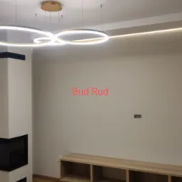 Nowoczesny salon we Wrocławiu z kominkiem, drewnianą podłogą i szafką RTV, oświetlony okrągłymi lampami LED i listwą świetlną na suficie.