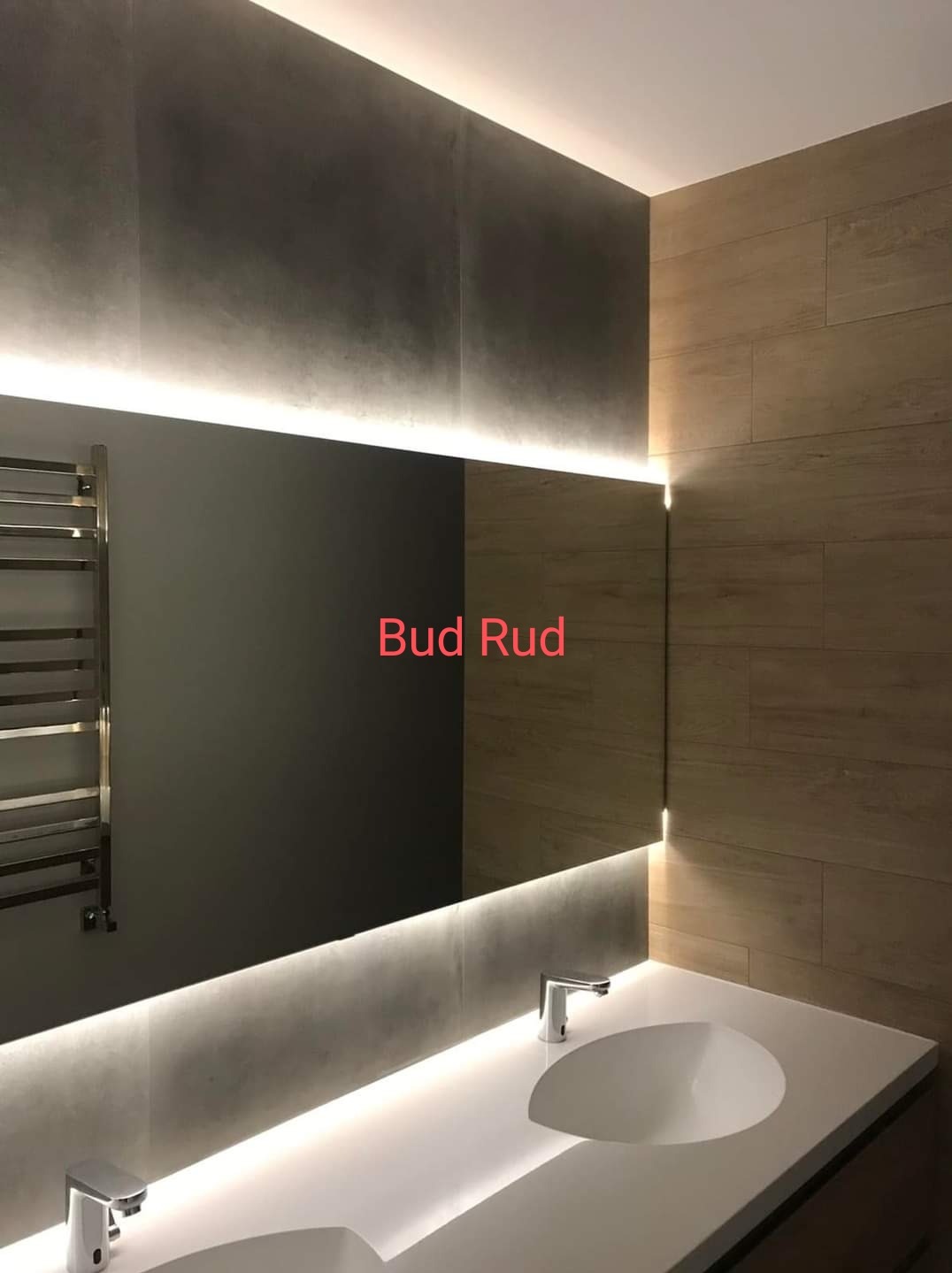 Nowoczesna łazienka z podświetlanym lustrem, szare płytki na ścianie i drewnopodobne panele, chromowany grzejnik drabinkowy po lewej stronie, biała umywalka z dwiema bateriami.