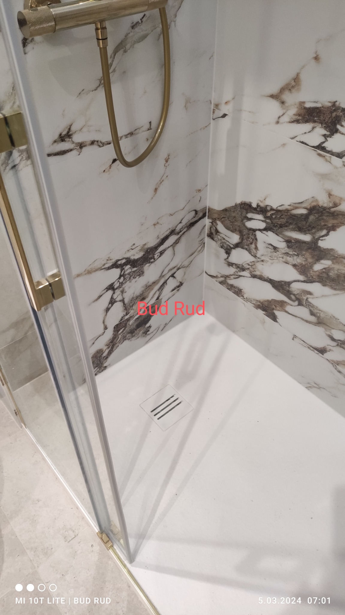 Nowoczesna kabina prysznicowa z marmurowymi panelami ściennymi i złotą armaturą, widoczny odpływ liniowy.