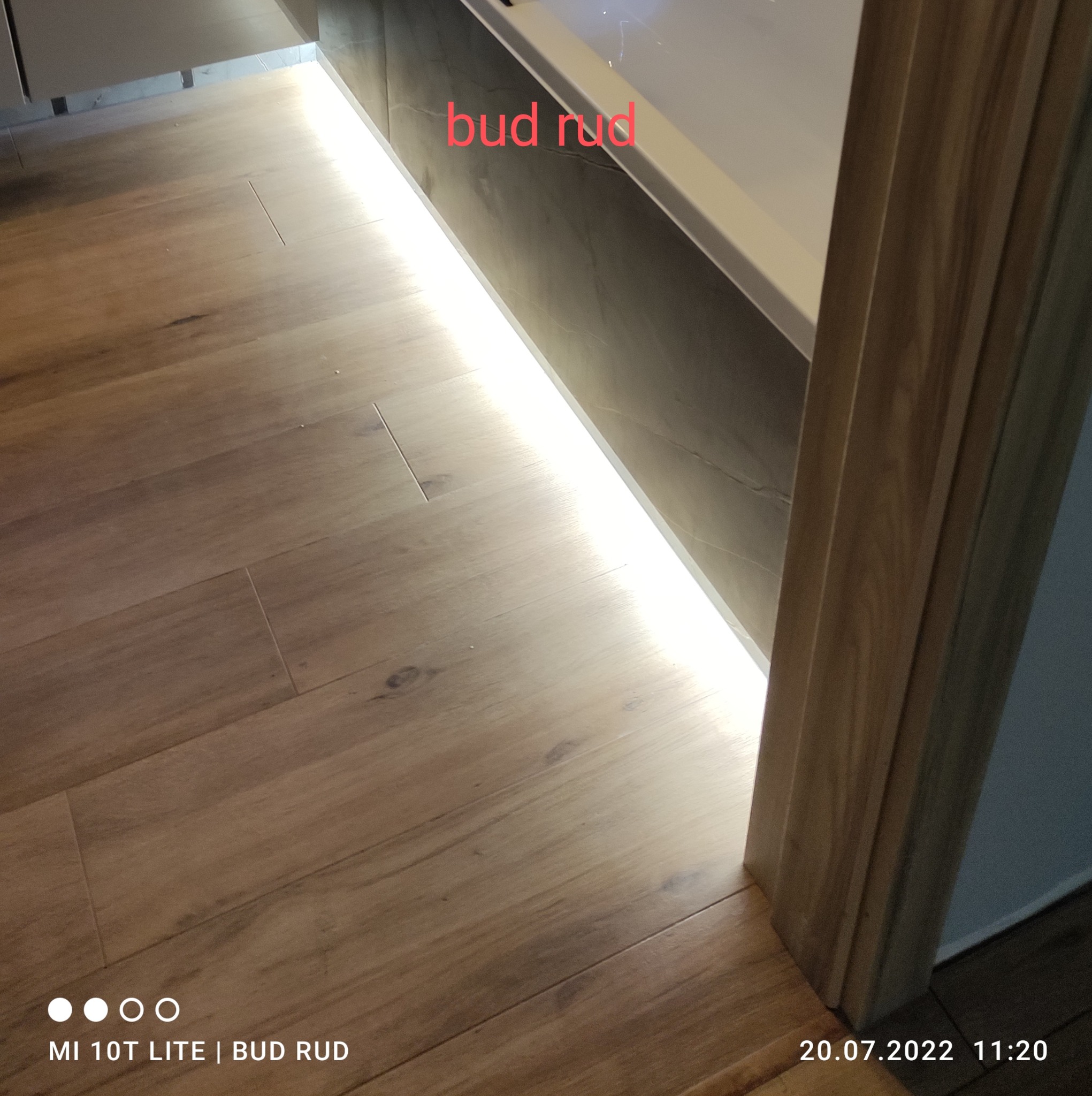 Ułożone panele podłogowe w łazience z oświetleniem LED pod wanną, widoczne fragmenty ściany z szarą fakturą i drewniana listwa przypodłogowa.