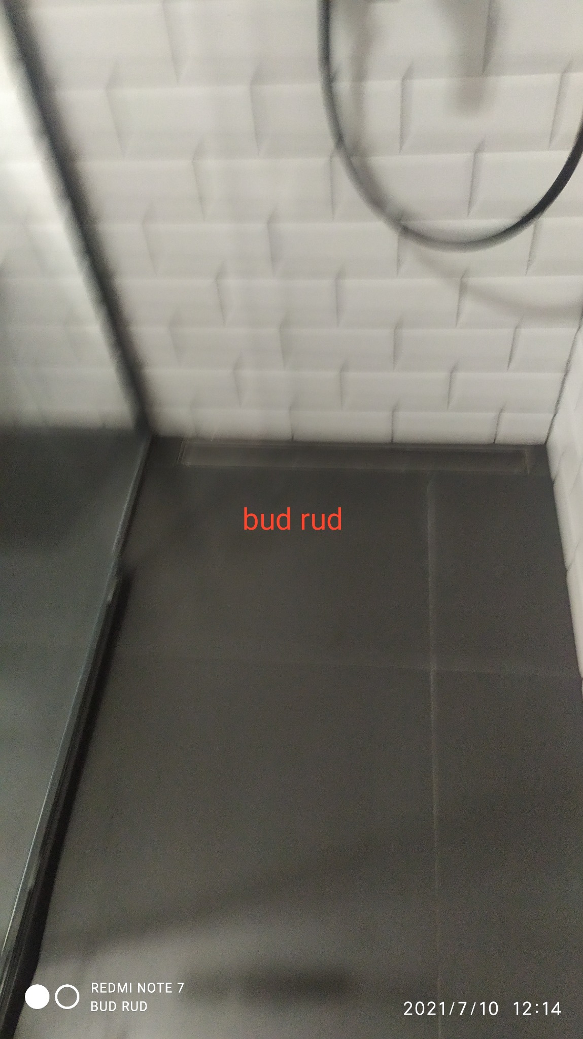 Ciemnoszare płytki podłogowe w łazience z białymi, wypukłymi płytkami na ścianie i widocznym odpływem liniowym.