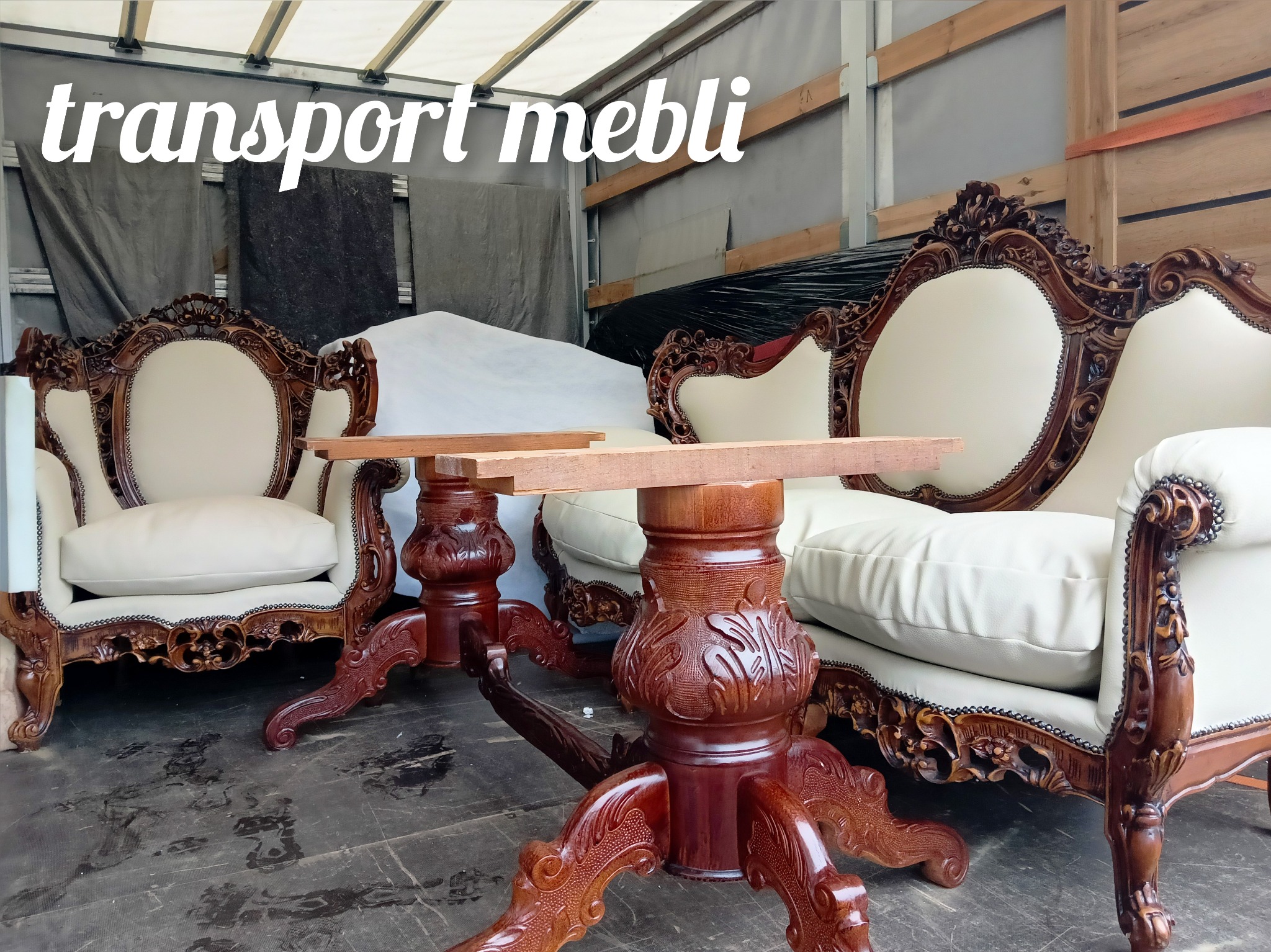 Wnętrze busa z załadowanym kompletem mebli w stylu barokowym: kremowa tapicerka sofy i fotela z rzeźbionymi, ciemnobrązowymi elementami drewnianymi oraz dwa okrągłe stoliki z dekoracyjnymi nogami...