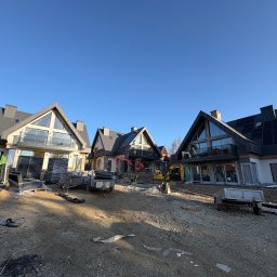 KB PROJEKT KACPER NOWAK - Trzy nowoczesne domy z panelami słonecznymi w trakcie budowy, z widocznymi maszynami budowlanymi i materiałami na placu budowy w słoneczny dzień.