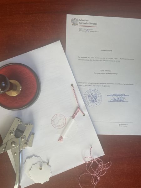 Dokument Ministerstwa Sprawiedliwości ze stemplem, sznurek, dziurkacz i stempel na drewnianym biurku, przygotowywane do poświadczenia.