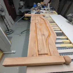 Drewniany, surowy front meblowy z ozdobnymi detalami, widoczny w warsztacie stolarskim, na stole roboczym obok narzędzi i innych elementów meblowych.