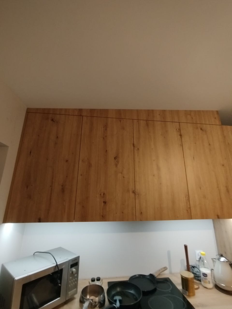 Wiszące szafki kuchenne z drewnopodobnym fornirem, widok od dołu, z widocznymi sprzętami AGD na blacie.