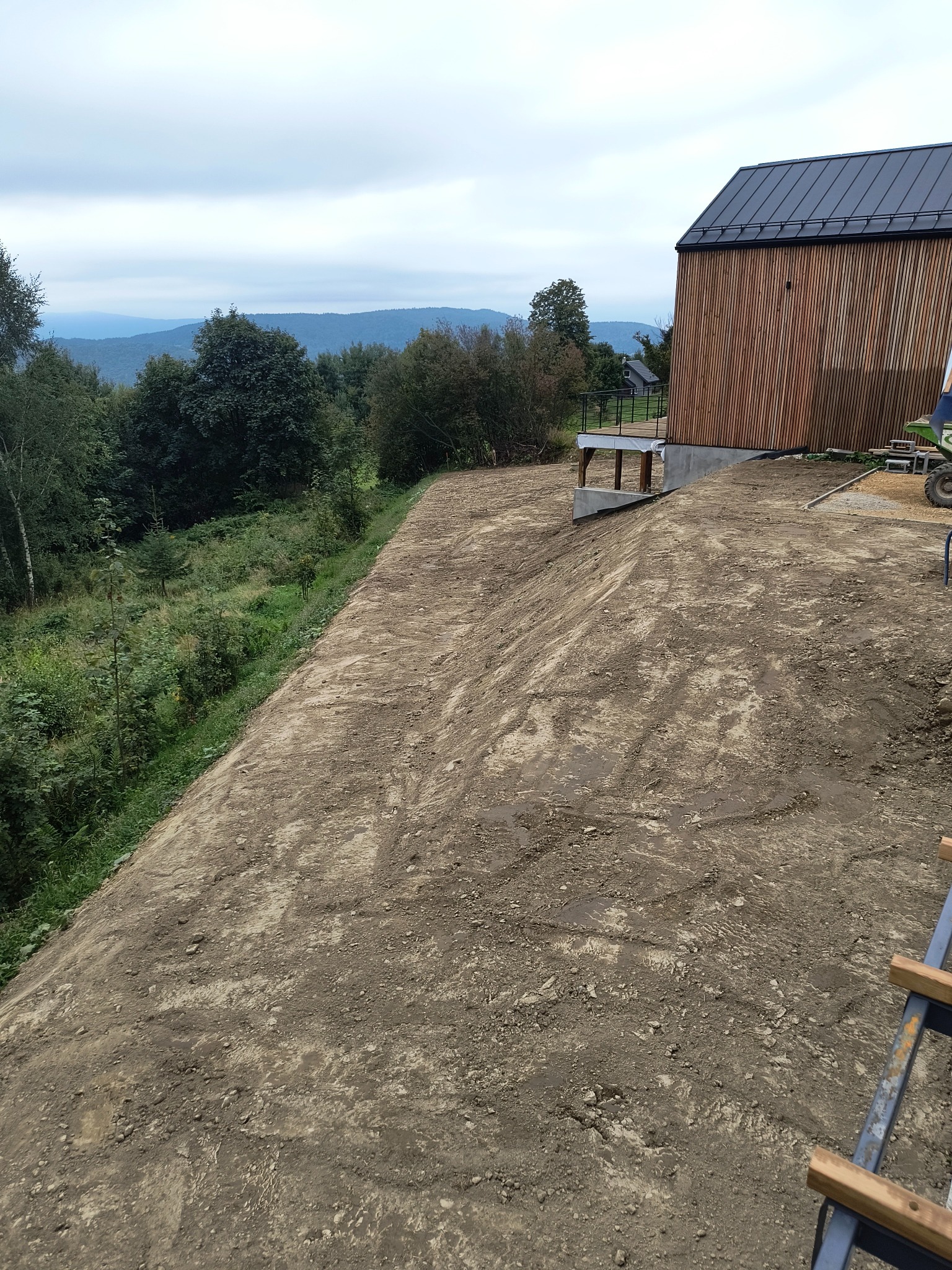 Przygotowany teren pod budowę domu z widocznymi śladami po maszynach, w tle góry i las.