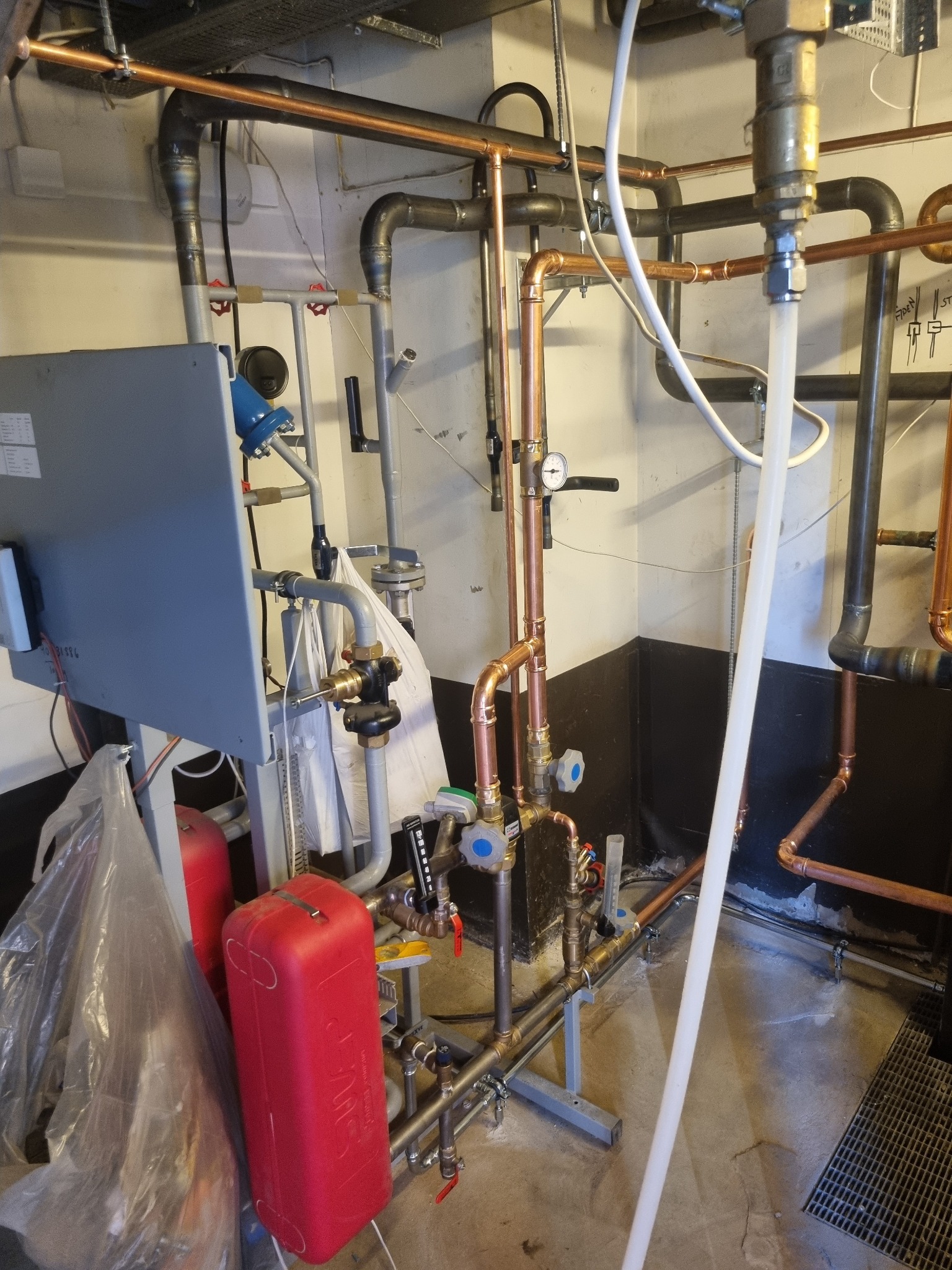 Złożona instalacja hydrauliczna z rur miedzianych i stalowych, widoczna w piwnicy w Błędowej Tyczyńskiej, obejmująca liczne zawory, manometry i zbiorniki, z elementami w trakcie montażu lub po...