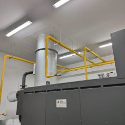 Adrian Kiełbasa - Nowoczesna instalacja gazowa z żółtymi rurami doprowadzającymi gaz do pieca kremacyjnego w czystym, przemysłowym pomieszczeniu.