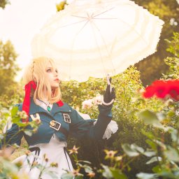 Herbata Photo - Kobieta w kostiumie Violet Evergarden z blond peruką i koronkowym parasolem, pozująca w ogrodzie różanym.