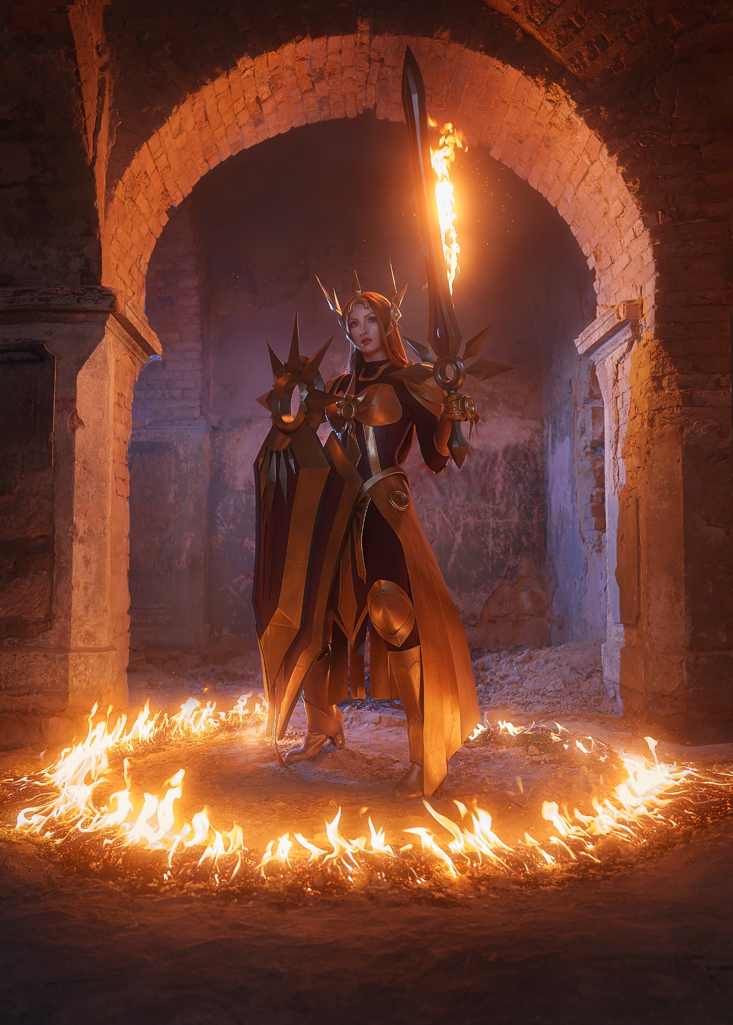 Kobieta w kostiumie wojowniczki z płonącym mieczem, otoczona kręgiem ognia w ceglanym łukowatym przejściu.
