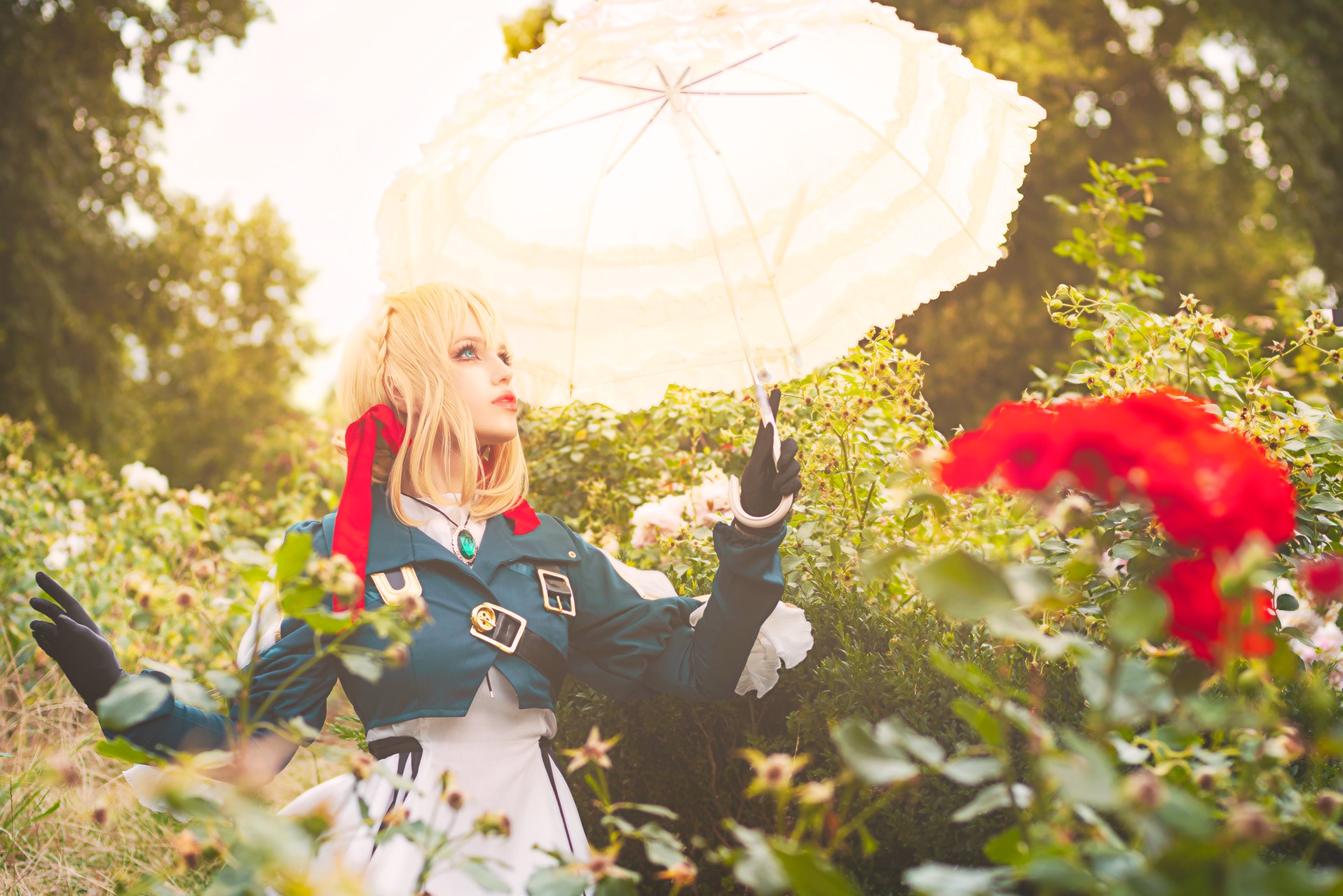 Kobieta w kostiumie Violet Evergarden z blond peruką i koronkowym parasolem, pozująca w ogrodzie różanym.