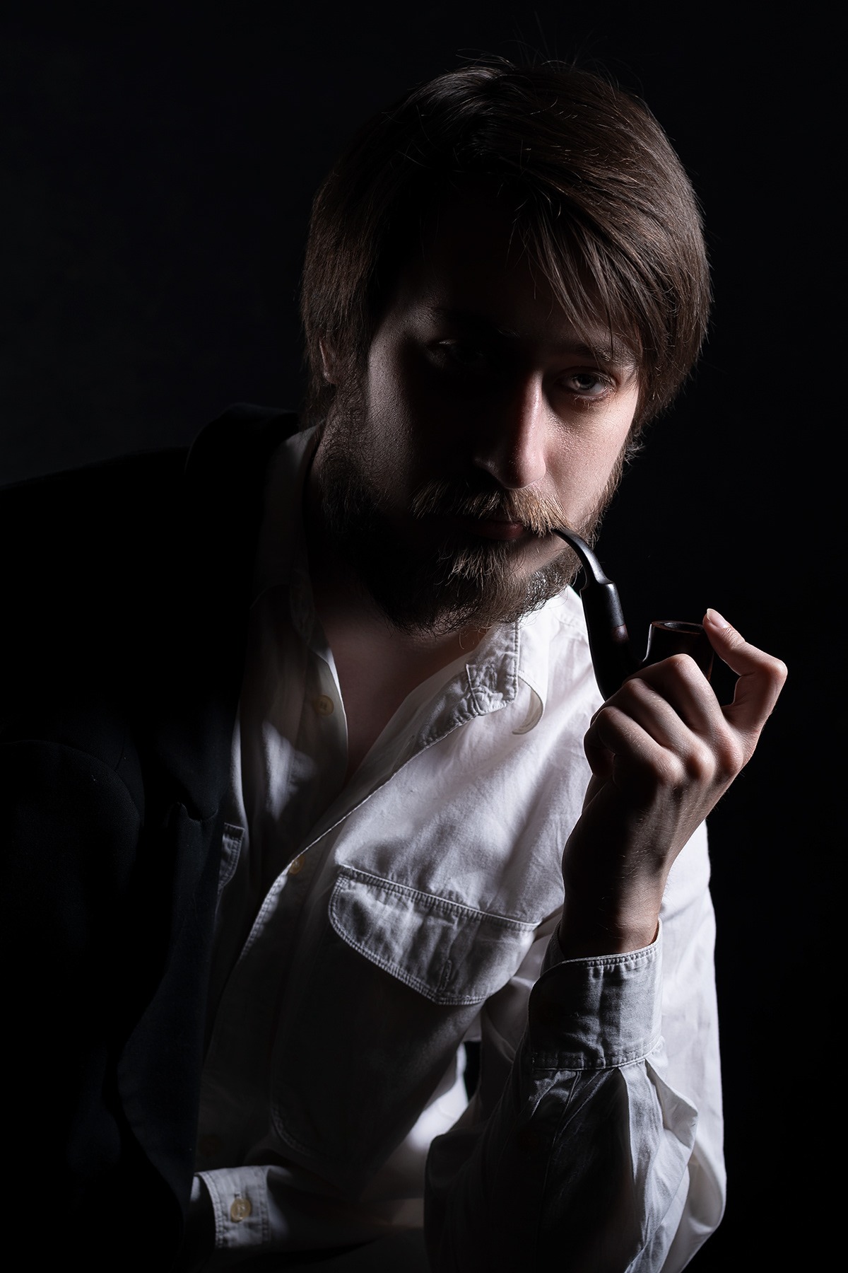 Portret mężczyzny z brodą w Toruniu, trzymającego fajkę w dłoni, w białej koszuli i marynarce na ciemnym tle.