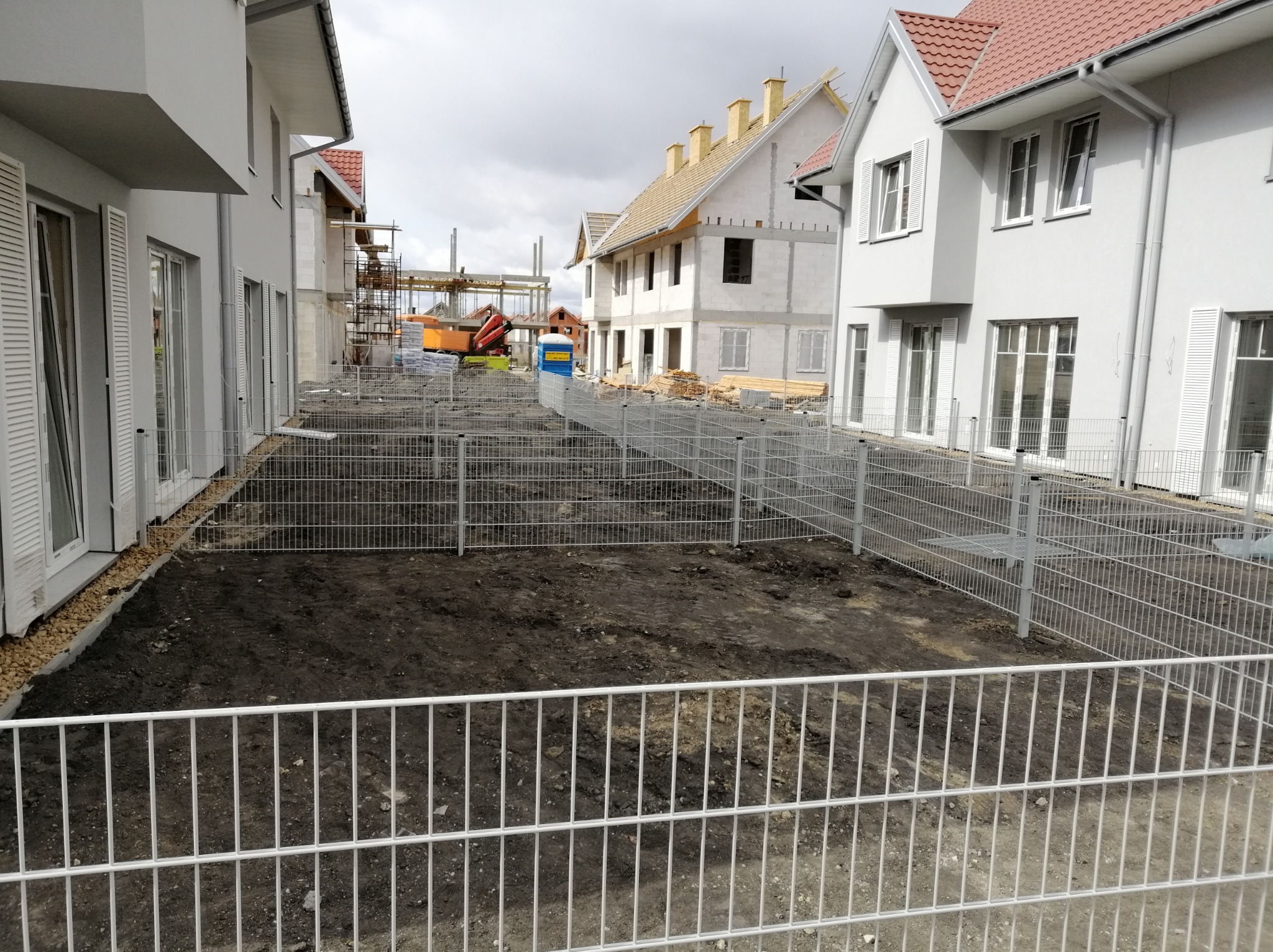 Montaż tymczasowego ogrodzenia z paneli metalowych na placu budowy pomiędzy nowymi domami jednorodzinnymi w trakcie budowy.