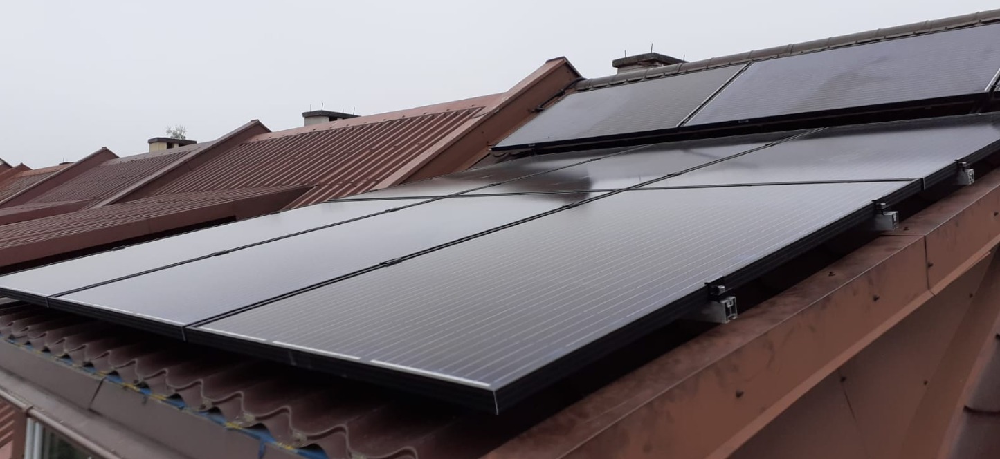 Panele słoneczne zamontowane na brązowym, blaszanym dachu domu jednorodzinnego w pochmurny dzień.