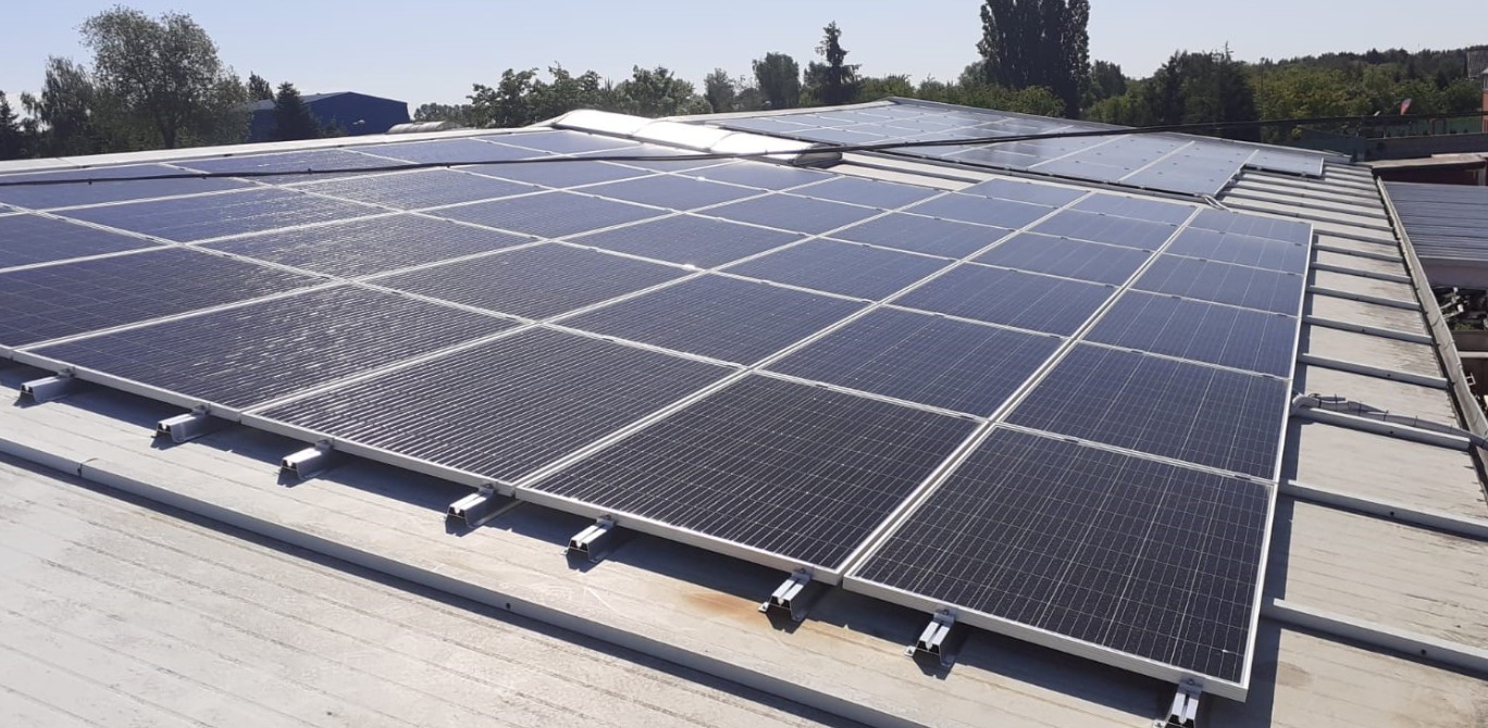 Rząd paneli słonecznych zamontowanych na dachu płaskim z widocznymi mocowaniami, instalacja w słoneczny dzień.