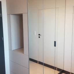Era meble Bogumił Woźniak - Jasnoszara zabudowa wnęki z lustrzanymi drzwiami przesuwnymi, widoczne szuflady i otwarta półka, minimalistyczny design.